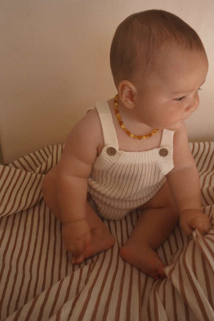 Baby wearing the Freckles The Label Chunky Button Romper in Oat, side view